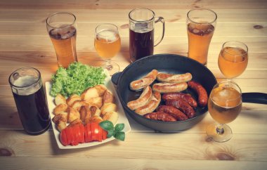 Bira, ızgara sosis ve ahşap masa üzerinde kavrulmuş patates