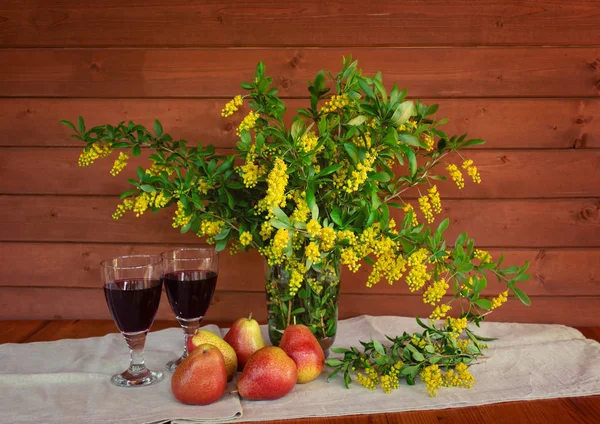 Fleurs jaunes d'épine-vinette dans un vase en verre, verres de vin rouge et poires fraîches sur table en bois — Photo