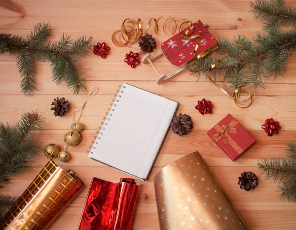Prázdný zápisník, jedlové větve, balicí role, dárková krabice a vánoční ozdoby na dřevěném pozadí. — Stock fotografie