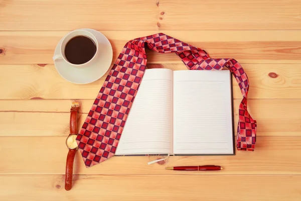 Öppnad dagbok, slips, kopp kaffe, klocka och penna på träbord. — Stockfoto