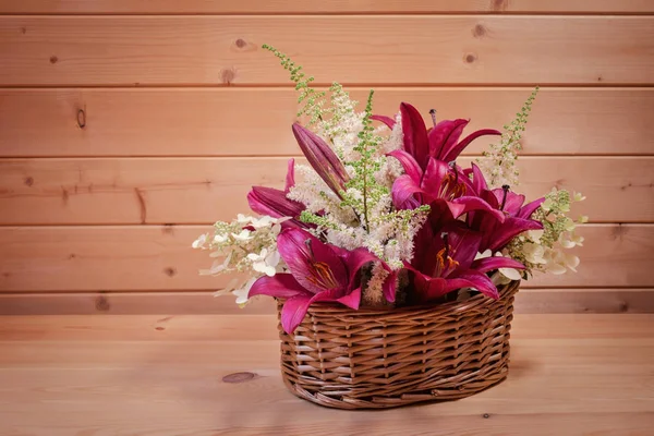 Cesto di vimini con gigli viola e astilbe bianco e fiori di ortensia su tavolo di legno. Focus selettivo . Foto Stock