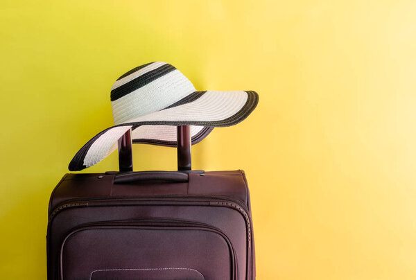 Brown suitcase and large beach hat on yellow background