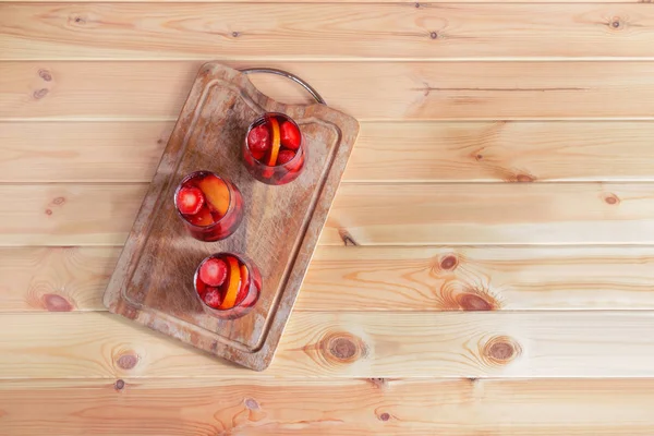 Hausgemachte erfrischende Frucht-Rotweinsangria in Gläsern auf Schneidebrett über rustikalem Holztisch. — Stockfoto