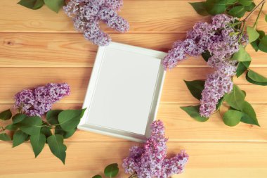 Ahşap arka planda leylak dalları ve beyaz çerçeve. Üst görünüm.