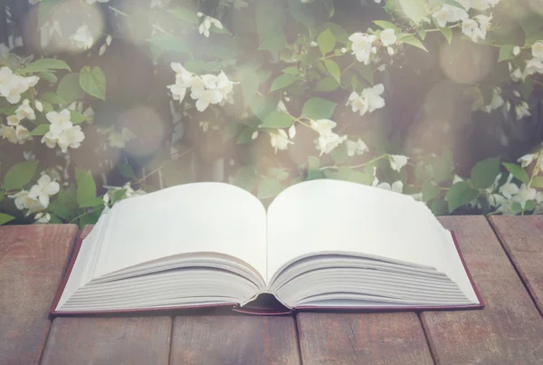 Libro aperto vuoto su tavolo di legno invecchiato su sfondo fiori di gelsomino fresco. Seleziona messa a fuoco . — Foto Stock