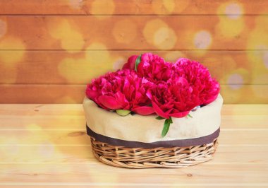 Hasır sepetin içinde, ahşap masada güzel kırmızı şakayık çiçekleri. Seçici odaklanma. Kopyalama alanı ile göster.