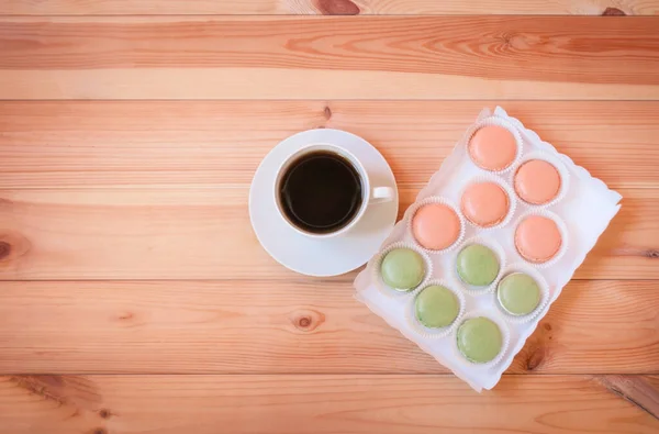 Cup of coffee and box of colorful macaroon cookies on wooden table. Top view, copy space.
