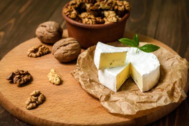 Ahşap arka planda ceviz çekirdekli Camembert veya Brie peyniri. Uzayı kopyala Penicillium camemberti 'nin tepesinde beyaz küf büyüyor.. 