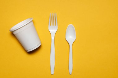 Sarı arka planda tek kullanımlık cam, kaşık ve mısır nişastası. Biyolojik çözünebilir çevre dostu piknik masaları. İzole et. Plastiğin modern biyomateryallerle değiştirilmesi.