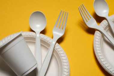 Sarı arka planda mısır nişastasından yapılmış iki adet tek kullanımlık yemek takımı. Piknik için çevre dostu tabak, cam, kaşık ve çatal. İzole et. Plastiğin modern malzemelerle değiştirilmesi