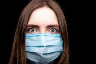 Siyah arka planda tıbbi maskeli genç bir kız. İzole et. Yakın plan portre. Virüslere ve enfeksiyonlara karşı koruma. Gözlerde Coronavirus duyguları var. Yorgunluk, korku.