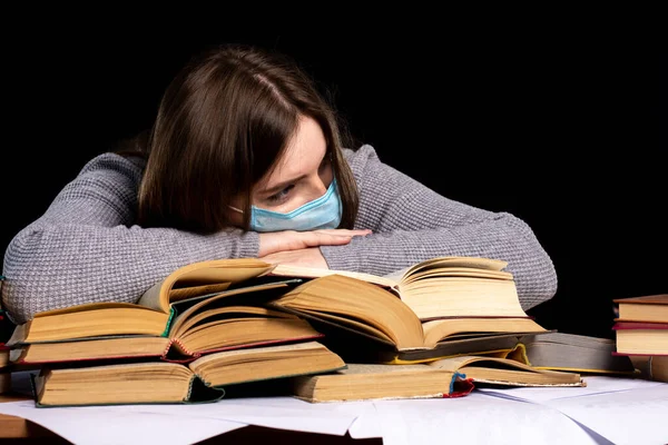 机の上の医療マスクの少女が本の上に頭を置いた 隔離における距離学習の難しさです 感染保護 — ストック写真