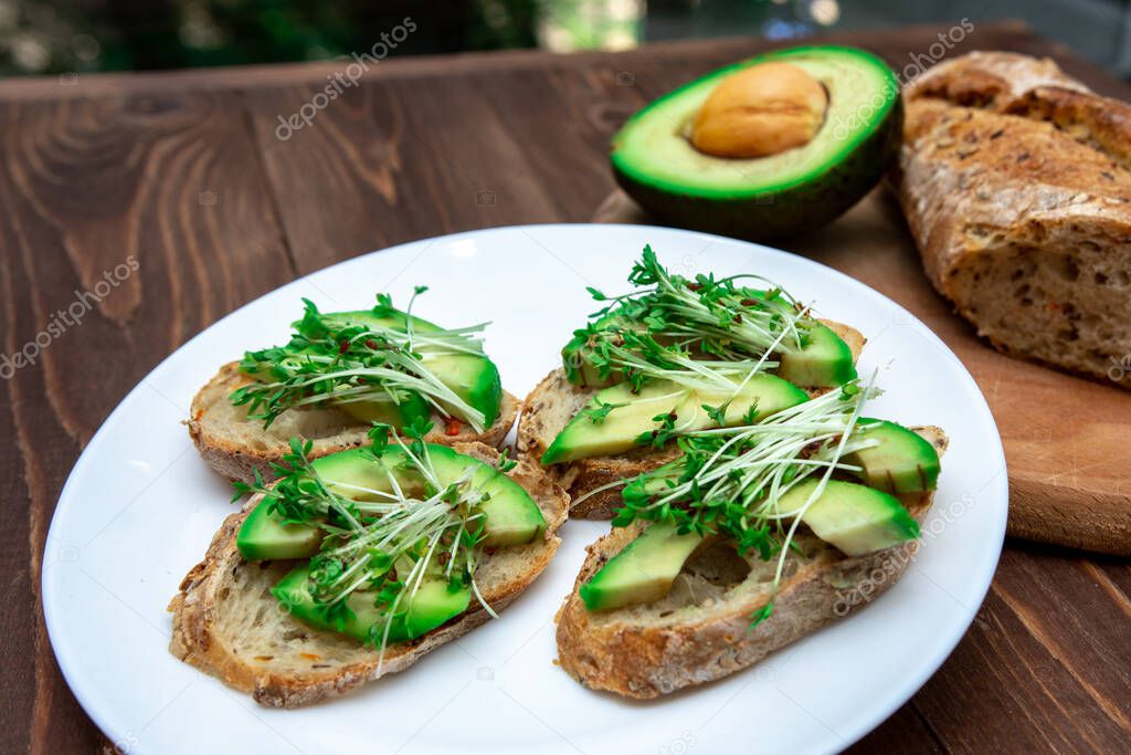  sandwiches with microgreens and avocado on a white plate on a wooden table. Clean eating healthy food concept. Top view. 