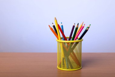 Masanın üzerinde mavi bir duvarın arkasında çok renkli kalemler olan sarı kırtasiye kupası..