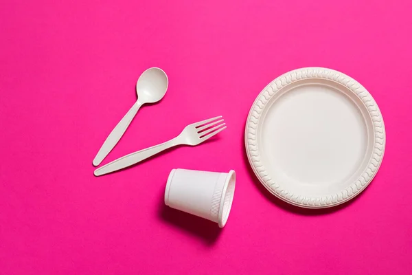 Pembe bir arka planda biyolojik olarak ayrıştırılabilir tek kullanımlık sofra takımı. Kaşık, çatal, tabak, bir bardak mısır nişastası. Çevre dostu. Plastiğin yerine modern ekolojik biyomateryaller.