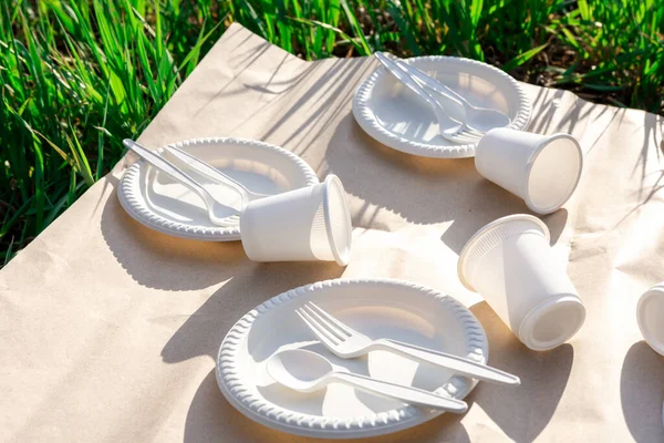 biodegradable disposable tableware from environmentally friendly materials. spoons, forks, glasses and plates of corn starch in nature on craft paper. shadow from the grass. close-up