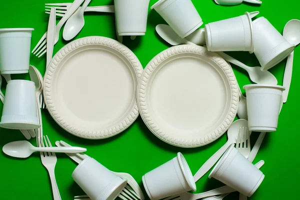 biodegradable eco-friendly disposable tableware on a green background. forks, spoons, glasses, and cornstarch plates. isolate. modern replacement for plastic. biomaterials. place for text.