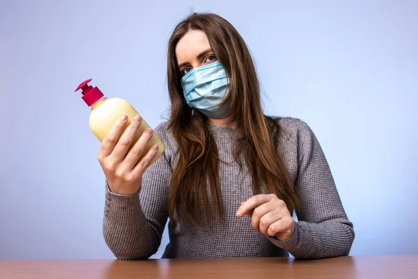 a young girl in a medical mask holds a bottle with an antiseptic or cream in her hands. sanitizer for the treatment of bacteria. skin hydration. infection protection. quarantined precautions