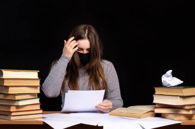 Siyah maskeli kız masada dokümanları okuyor. Bir yığın kitap. Karantinaya alınmış iş.