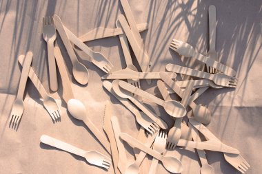 disposable forks and spoons from environmentally friendly materials on craft paper in nature. shadow from the grass. picnic with wooden biodegradable utensils. place for text clipart