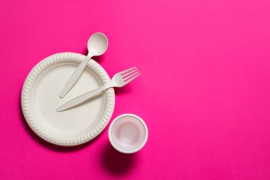 Tek kullanımlık ayrışan çatal, kaşık, cam ve pembe arka planda bir tabak mısır nişastası. Çevre dostu yemekler. İzole et. mesaj için yer. modern eko plastik değiştirme