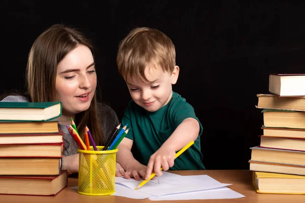 Молодой Учитель Помогает Маленькому Мальчику Писать Школьный Стол Книгами Банкой — стоковое фото