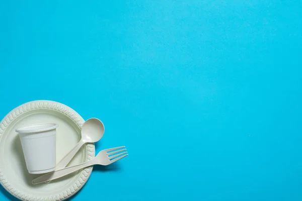 disposable eco-friendly fork, spoon, plate and cup of corn starch on a blue background. biodegradable dishes made from modern materials. place for text. isolate.