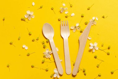 Kiraz çiçekleriyle çevrili sarı bir arka planda tahta çatal, kaşık ve bıçak. mesaj için yer. Çevre dostu