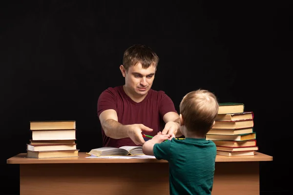 the little son ran to dad. young businessman sits at a table with books and documents. difficulties at home. quarantined remote work. child takes a pencil from the desk