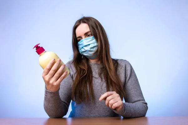 a young girl in a medical mask looks at a bottle with an antiseptic or cream in her hands. a disinfectant for treating bacteria. skin hydration. infection protection. quarantine precautions