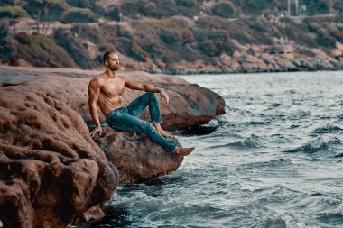 Kaslı adam kayalıkların yanında oturur.