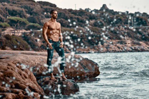 Kayalıkların yanında duran kaslı adam.