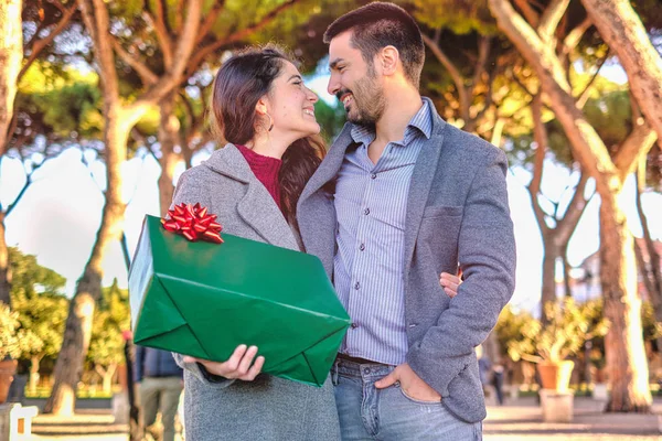 Young Attractive Couple Sharing Christmas Or Valentines Day Gift In The Park during the day time - love engage surprise conceptual moment — Stock Photo, Image