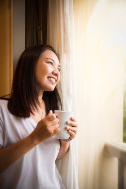 Asyalı kız pencereden dışarı bak rahatlatıcı kahve tutun