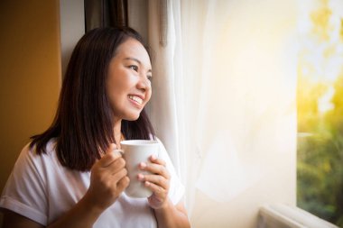 Asyalı kız pencereden dışarı bak rahatlatıcı kahve tutun