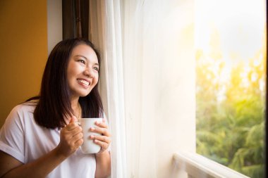 Asyalı kız pencereden dışarı bak rahatlatıcı kahve tutun
