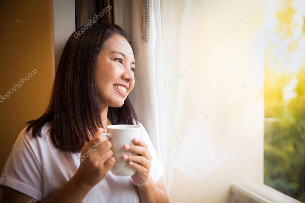 Asian girl hold cup of coffee relaxing look outside window