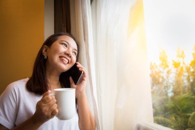 Asyalı kız tutun bir fincan kahve ve smartphone kullanarak 