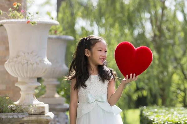 Liten flicka i vit klänning holding rött hjärta kudde, Valentine — Stockfoto