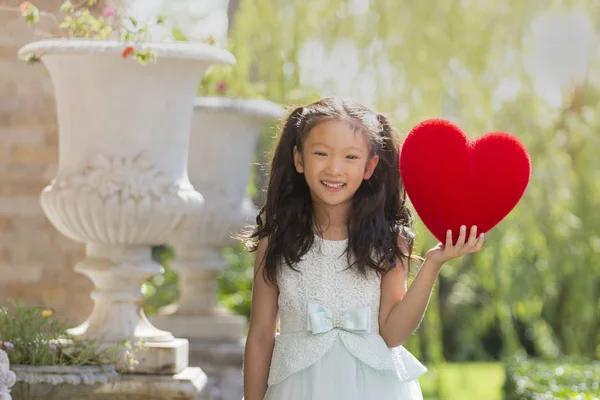 Liten flicka i vit klänning holding rött hjärta kudde, Valentine — Stockfoto