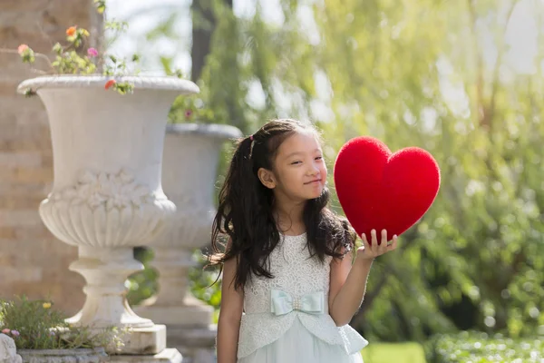 Liten flicka i vit klänning holding rött hjärta kudde, Valentine — Stockfoto