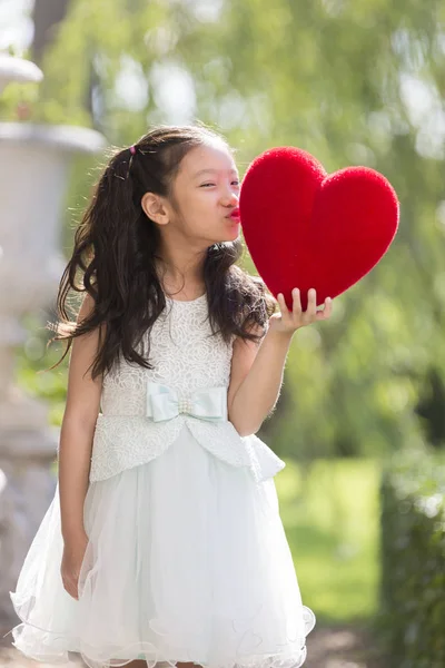 Little girl in white dress kissing red heart pillow concept for — Stock Photo, Image