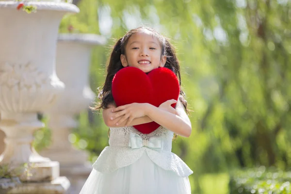 Lille pige i hvid kjole knus rødt hjerte pude koncept for vale - Stock-foto
