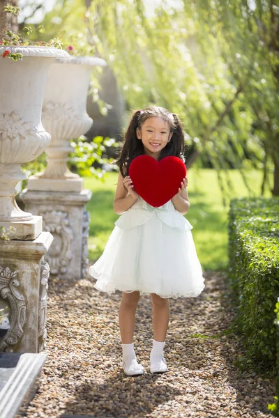 Liten flicka i vit klänning holding rött hjärta kudde, Valentine — Stockfoto