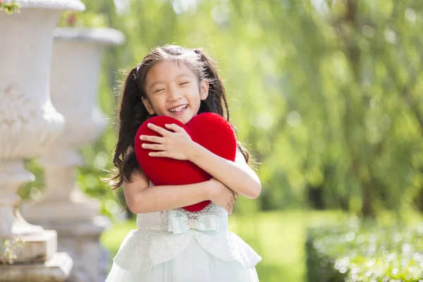 Kislány fehér ruhában piros szív párna koncepció vale ölelés — Stock Fotó