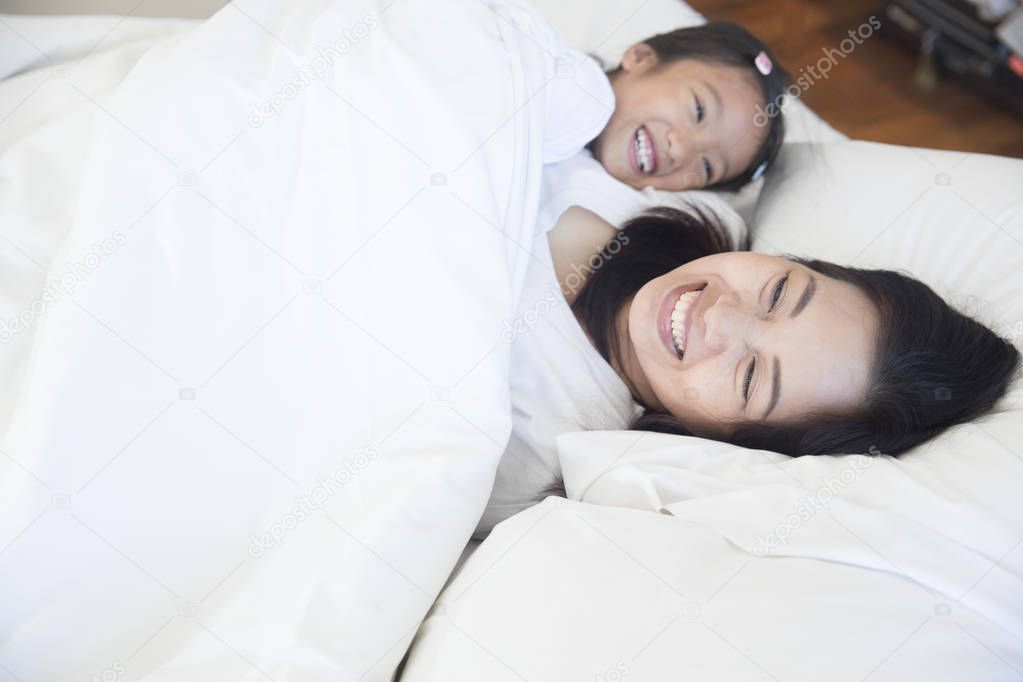 Happy Asian mother and daughter relaxing and sleeping on white b