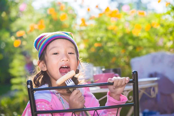 Piccola ragazza asiatica godere di mangiare pane per la prima colazione in giardino — Foto Stock
