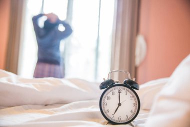 Çalar saat ile kadın windo yanında bulanık uyan beyaz yatakta