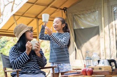 Asyalı anne ve kızı kamp alanında içki içiyorlar.