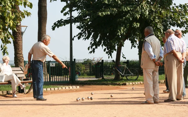 Antibes France 13. Oct 2008.  Petanque game on the beach promenade. The player points to the target. The audience is watching with their arms folded back.  Serious, respectable retirees.